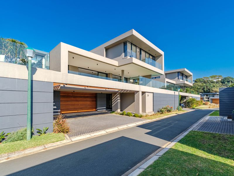 Modern townhouse exterior featuring a sleek architectural design, glass balustrades, and a spacious paved driveway with a timber garage door.