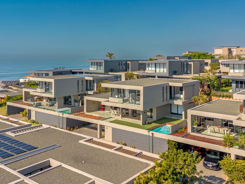 Aerial view of a modern townhouse complex featuring contemporary architecture, private swimming pools, solar panels, and scenic coastal views.