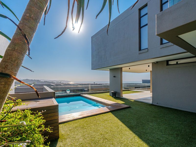 Modern townhouse exterior featuring a private swimming pool, timber decking, artificial lawn, and a covered patio with scenic coastal views.
