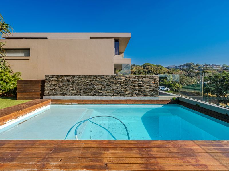 Modern outdoor pool area featuring timber decking, a stone-clad feature wall, and a glass balustrade overlooking the surrounding landscape.