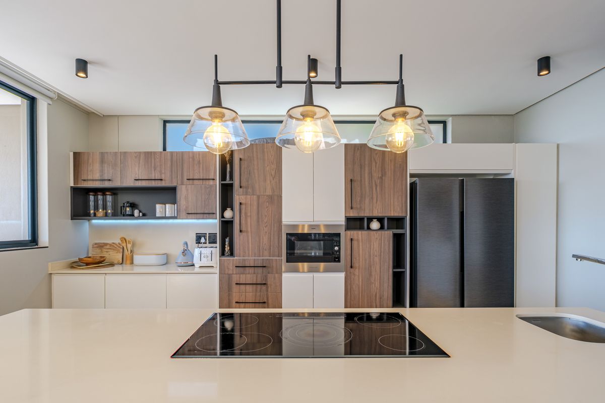 Modern kitchen featuring two-tone cabinetry, stone countertops, integrated appliances, induction cooktop, and stylish pendant lighting over the central island.