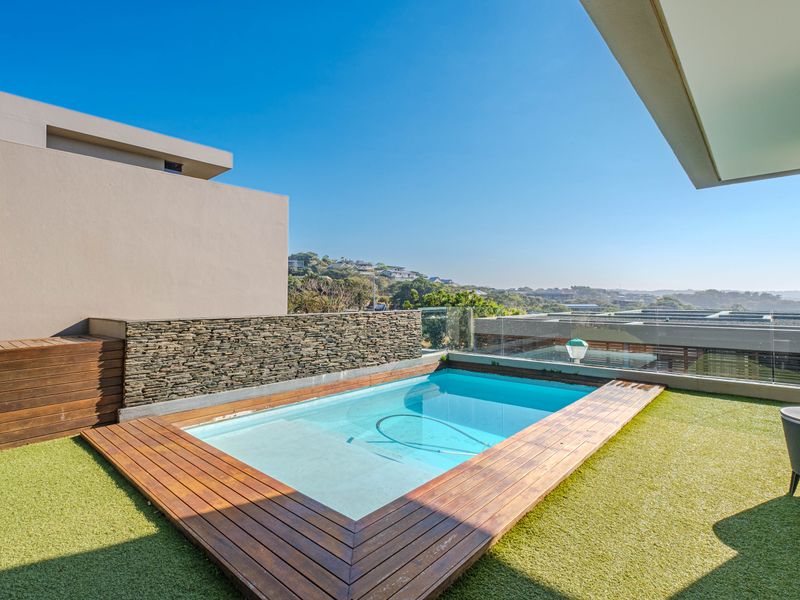 Elevated pool area featuring timber decking, a stone feature wall, and glass balustrades with scenic views.