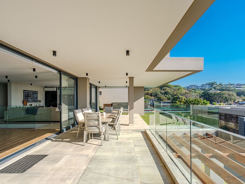 Spacious covered balcony featuring modern glass balustrades, recessed lighting, and seamless access to the interior living area through large sliding glass doors.