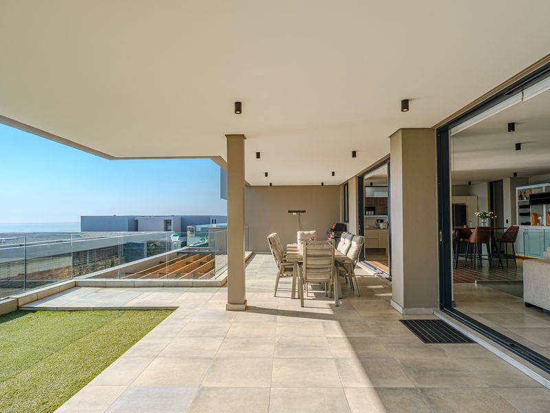 Spacious covered balcony featuring tiled flooring, glass balustrades, and seamless indoor-outdoor flow through large sliding doors, offering an ideal space for alfresco dining.