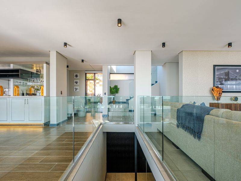 Modern open-plan living area featuring a glass balustrade overlooking a staircase, with sleek built-in cabinetry and recessed ceiling lighting.