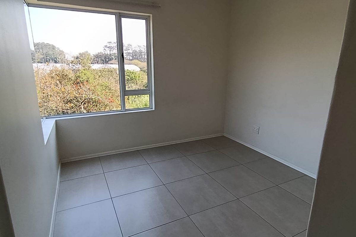 A bright, empty bedroom featuring neutral tiled flooring and a large window with natural light and exterior views.