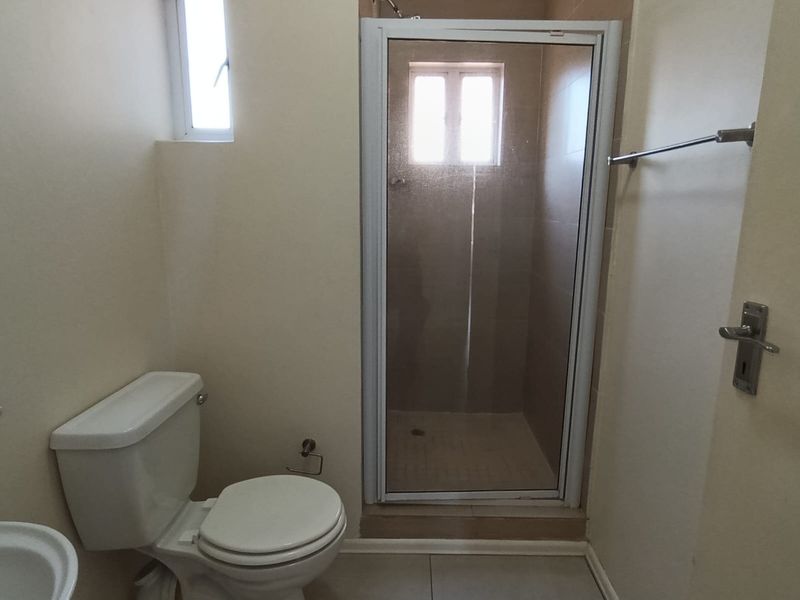 A functional bathroom featuring a shower enclosure, toilet, and tiled flooring, offering a clean and neutral space ready for personal touches.