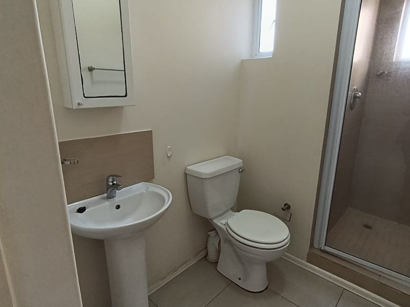 A functional bathroom featuring a pedestal basin, toilet, and a glass-enclosed shower with neutral tiled flooring.