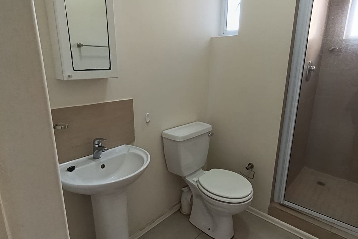 A functional bathroom featuring a pedestal basin, toilet, and a glass-enclosed shower with neutral tiled flooring.