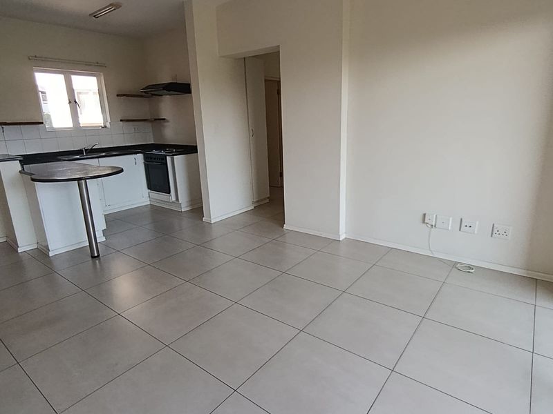 An open-plan living and kitchen area featuring neutral tiled flooring, modern cabinetry, a breakfast bar, and built-in kitchen appliances.