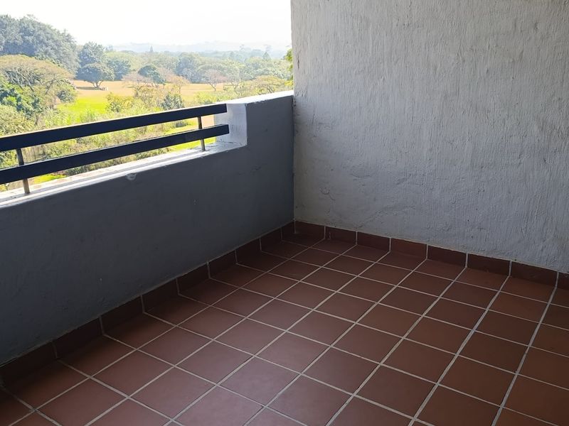 A simple balcony featuring terracotta-style floor tiles and a metal balustrade, offering an open view of the surrounding landscape.