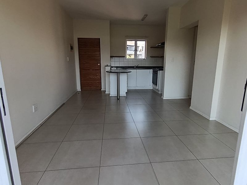 An open-plan living and kitchen area featuring neutral tiled flooring, modern cabinetry, a breakfast bar, and a built-in oven.