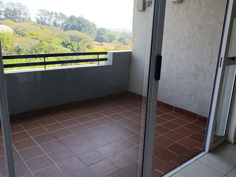 A private balcony featuring tiled flooring, a metal balustrade, and sliding glass door access, offering an open view of the surrounding greenery.