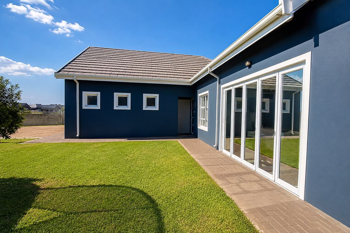 Rear view of the property featuring a well-maintained lawn, paved walkway, and modern bi-fold glass doors leading into the home.