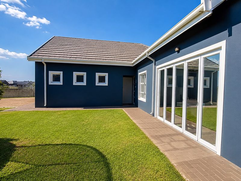 Rear view of the property featuring a well-maintained lawn, paved walkway, and modern bi-fold glass doors leading into the home.