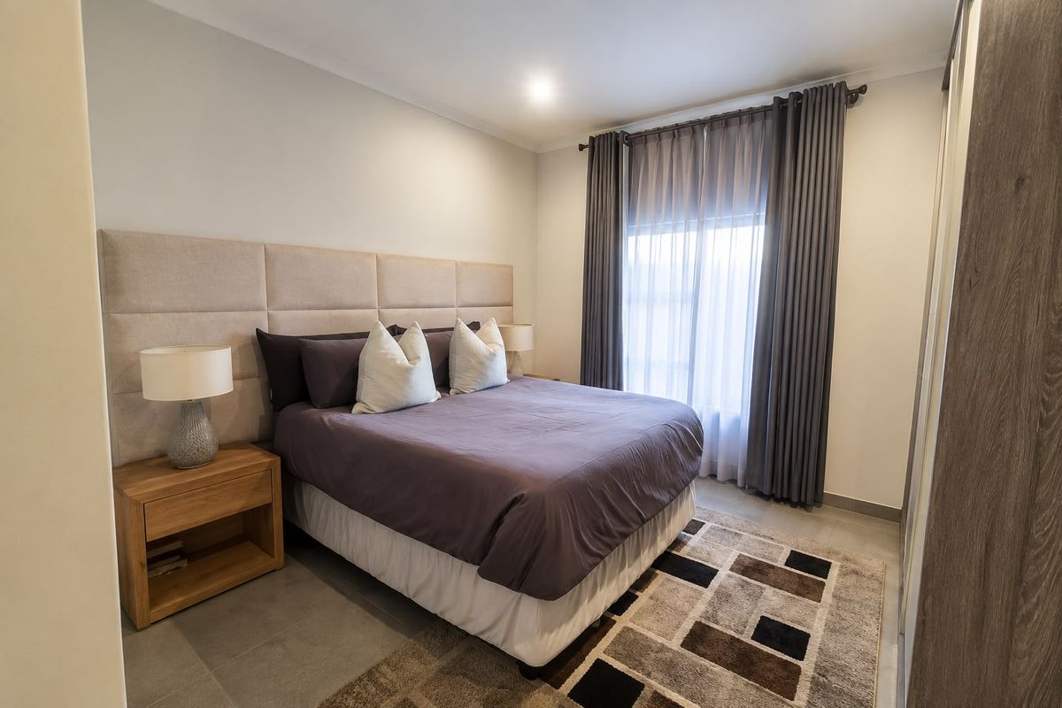 A well-maintained bedroom featuring tiled flooring, a large upholstered headboard, built-in wardrobe, and neutral finishes with floor-to-ceiling curtains.