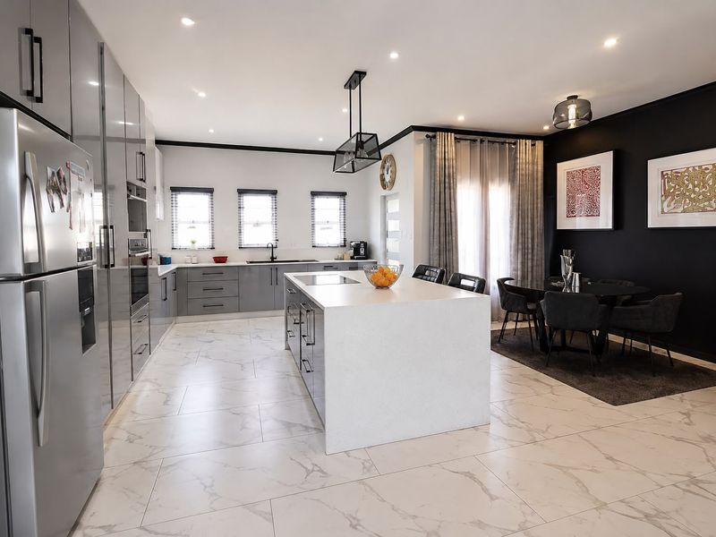 Modern open-plan kitchen and dining area featuring sleek grey cabinetry, a large central island with quartz countertops, and elegant marble-look floor tiles.