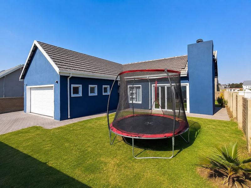 Rear view of a blue-painted house featuring a tiled roof, integrated garage, sliding glass doors, and a well-maintained lawn area.