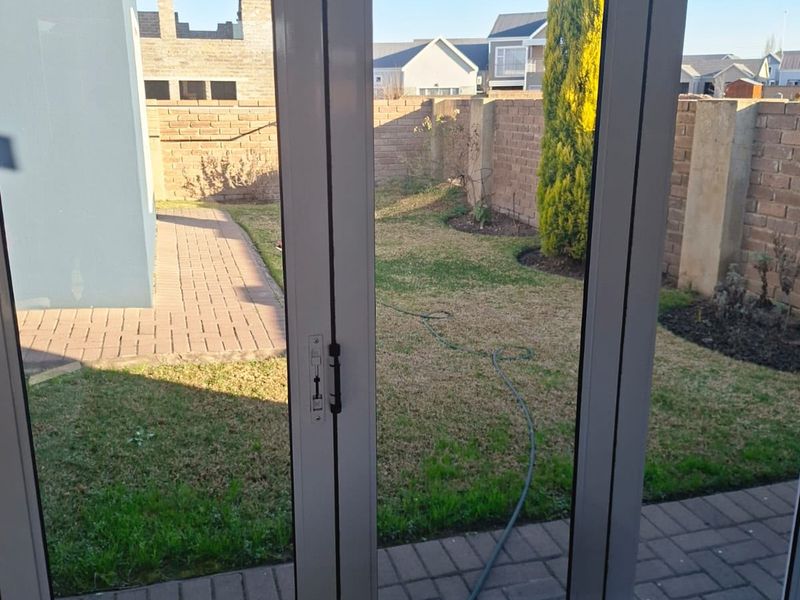 A view of the rear garden featuring a paved walkway, lawn, and brick boundary wall, accessed through modern aluminium framed glass doors.