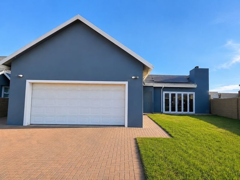 Modern single-story home featuring a double garage, paved driveway, solar panels, and bi-fold doors opening to a well-maintained lawn.