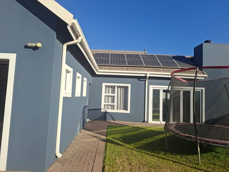 Rear exterior view of the house featuring a paved walkway, solar panels installed on the roof, and sliding glass door access.