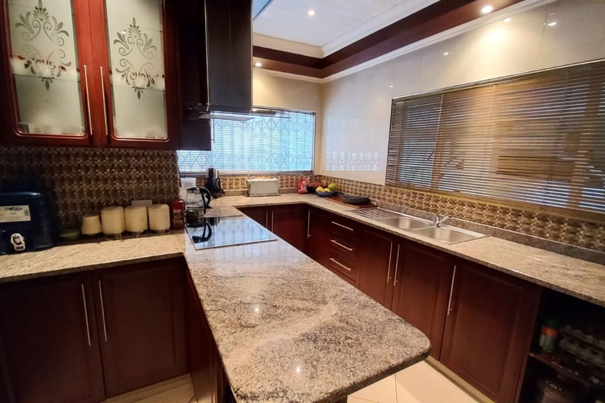 A well-maintained kitchen featuring dark wood cabinetry, granite countertops, a stainless steel sink, and a built-in electric hob with an extractor fan.