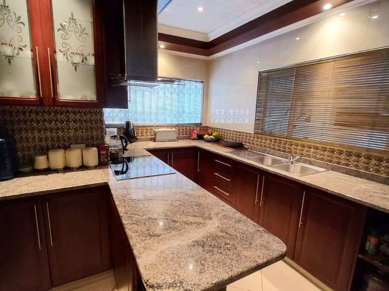 A well-maintained kitchen featuring dark wood cabinetry, granite countertops, a stainless steel sink, and a built-in electric hob with an extractor fan.