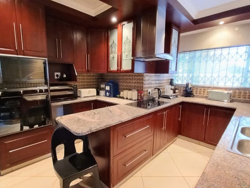 A well-maintained kitchen featuring dark wood cabinetry, granite countertops, built-in oven, extractor fan, and tiled flooring with security bars on the window.