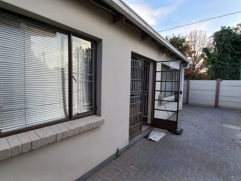 Rear exterior view of the property featuring a paved patio area, security gates, and perimeter walling.