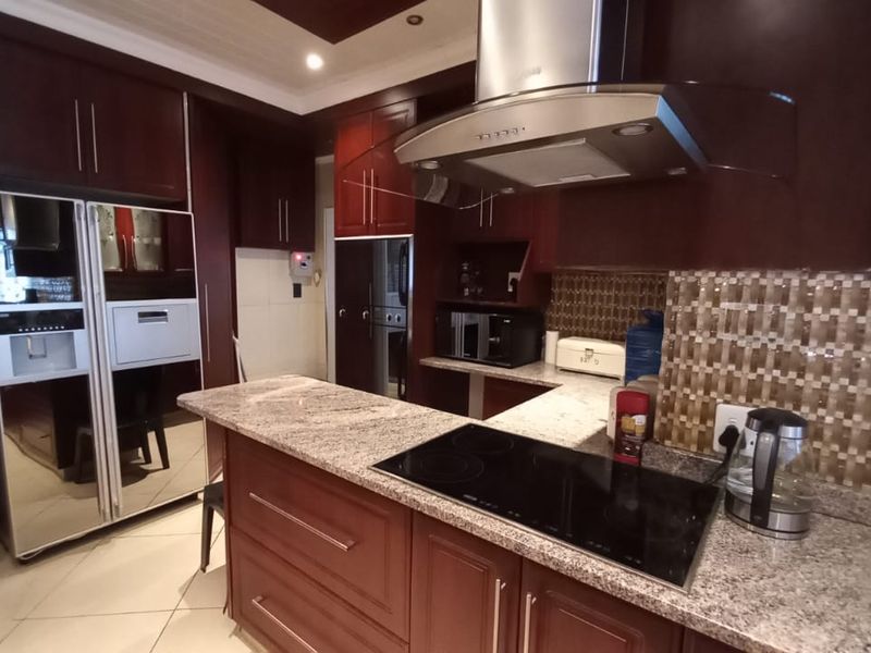 A well-appointed kitchen featuring dark wood cabinetry, granite countertops, a built-in electric hob, and a stainless steel extractor fan.