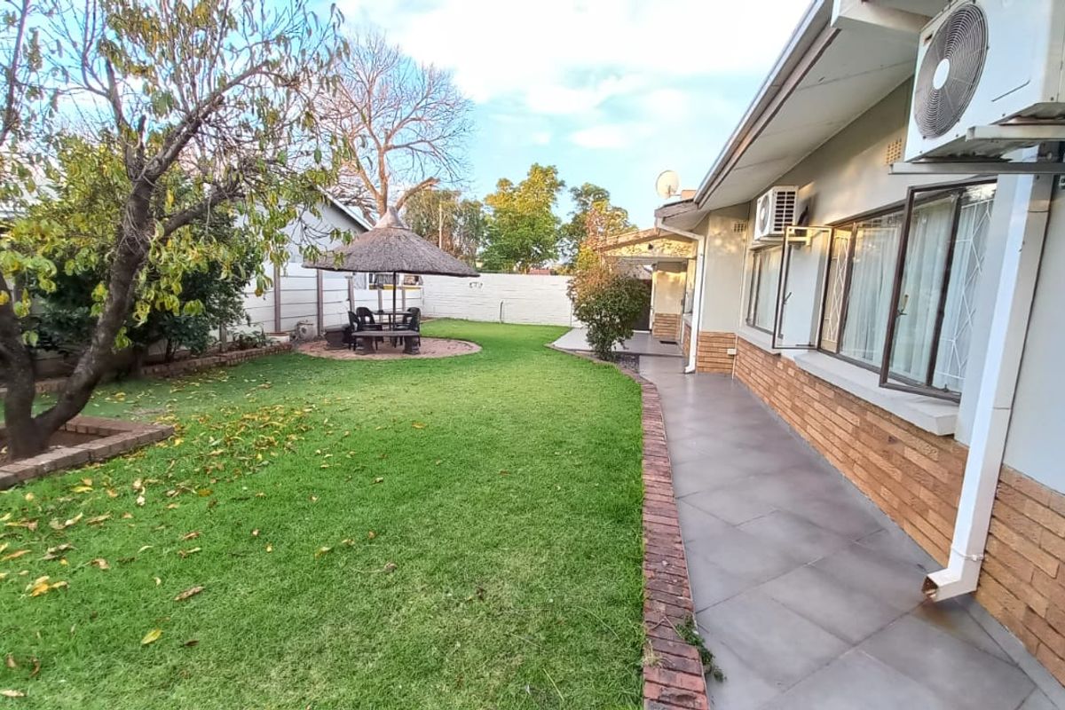 A well-maintained rear garden featuring a tiled patio, brick exterior walls, and a thatched lapa area, providing a functional outdoor space.