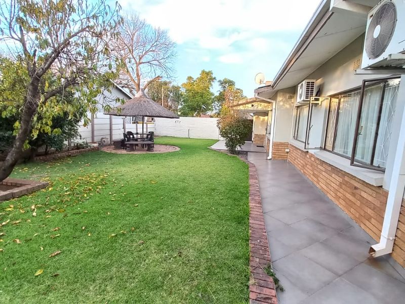A well-maintained rear garden featuring a tiled patio, brick exterior walls, and a thatched lapa area, providing a functional outdoor space.