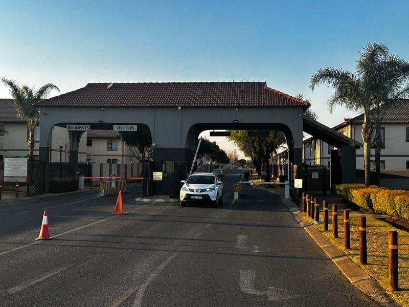 The main entrance to the townhouse complex featuring a secure gatehouse with boom gates for residents and visitors.
