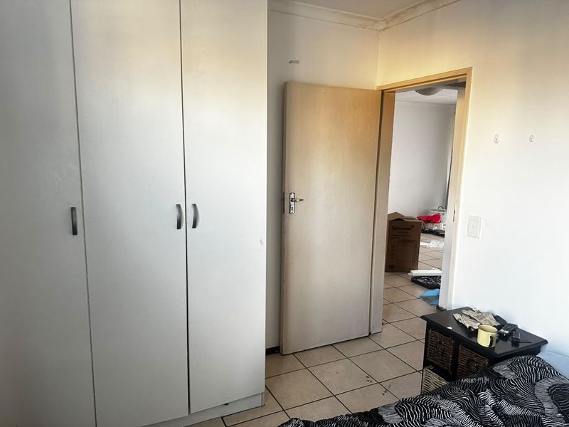 A bedroom featuring built-in wardrobes and tiled flooring, showing signs of wear and requiring cosmetic updates.
