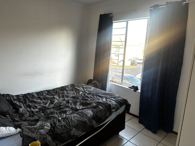 A functional bedroom featuring tiled flooring and a window with security bars, offering natural light and a view of the exterior.