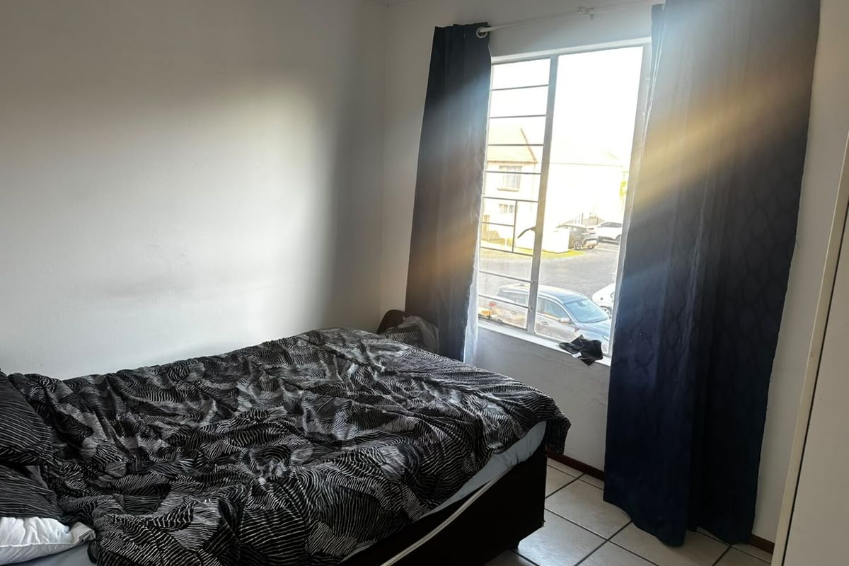 A functional bedroom featuring tiled flooring and a window with security bars, offering natural light and a view of the exterior.