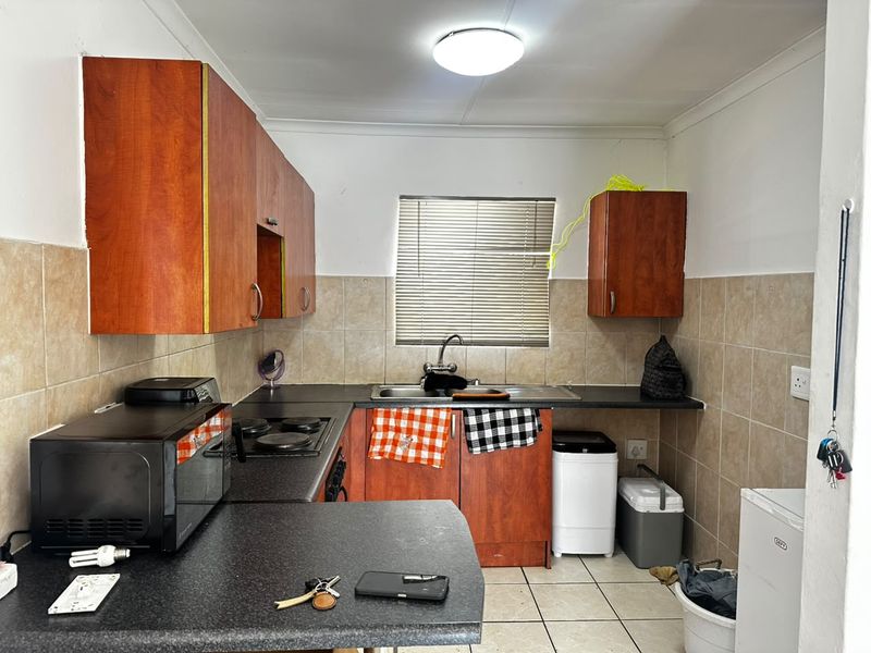 A functional kitchen featuring wooden cabinetry, laminate countertops, a stainless steel sink, and tiled finishes, offering a practical layout for daily meal preparation.
