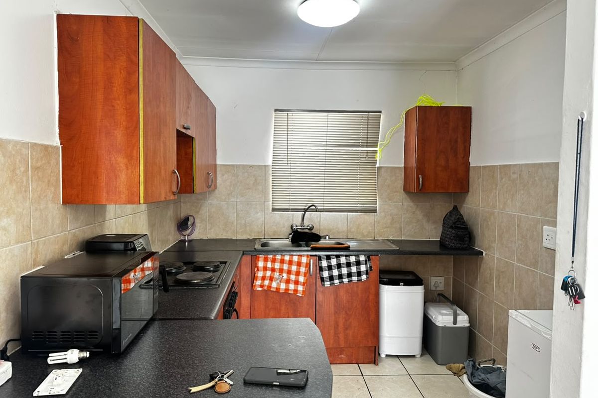 A functional kitchen featuring wooden cabinetry, laminate countertops, a stainless steel sink, and tiled finishes, offering a practical layout for daily meal preparation.