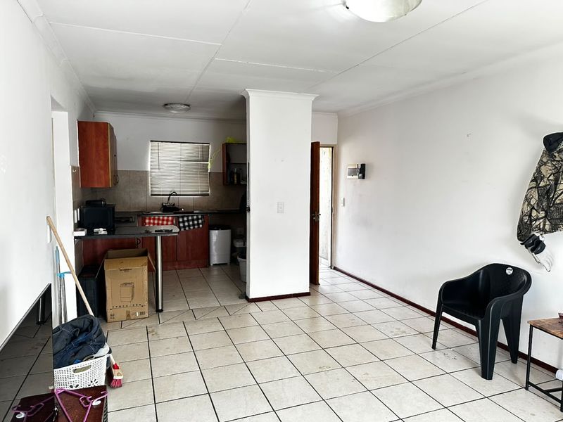 Open plan living area featuring tiled flooring and a compact kitchen with built-in cabinetry and sink, requiring cosmetic updates to enhance the space.