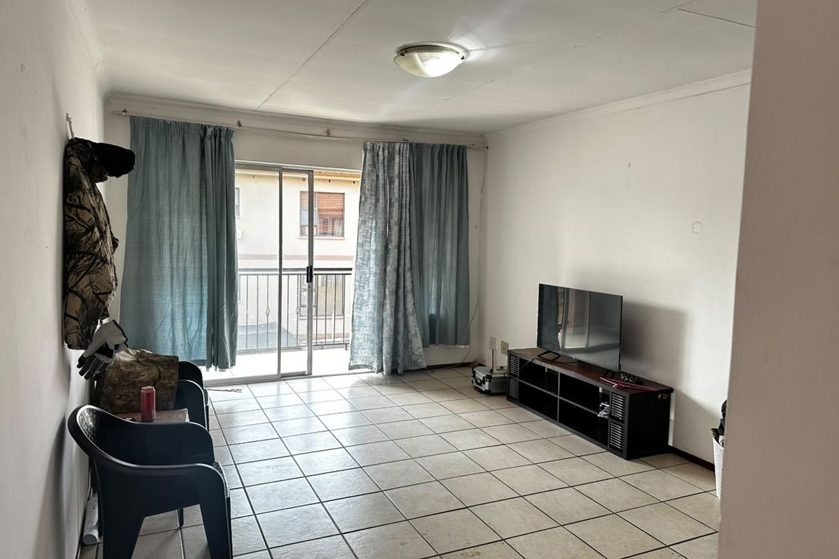 A living room featuring tiled flooring and a sliding glass door providing access to a balcony, offering potential for cosmetic updates.