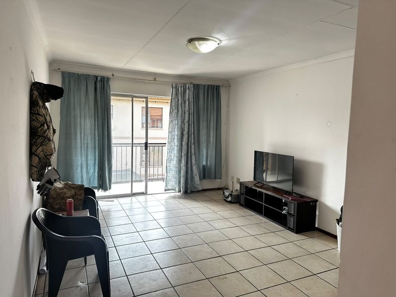 A living room featuring tiled flooring and a sliding glass door providing access to a balcony, offering potential for cosmetic updates.