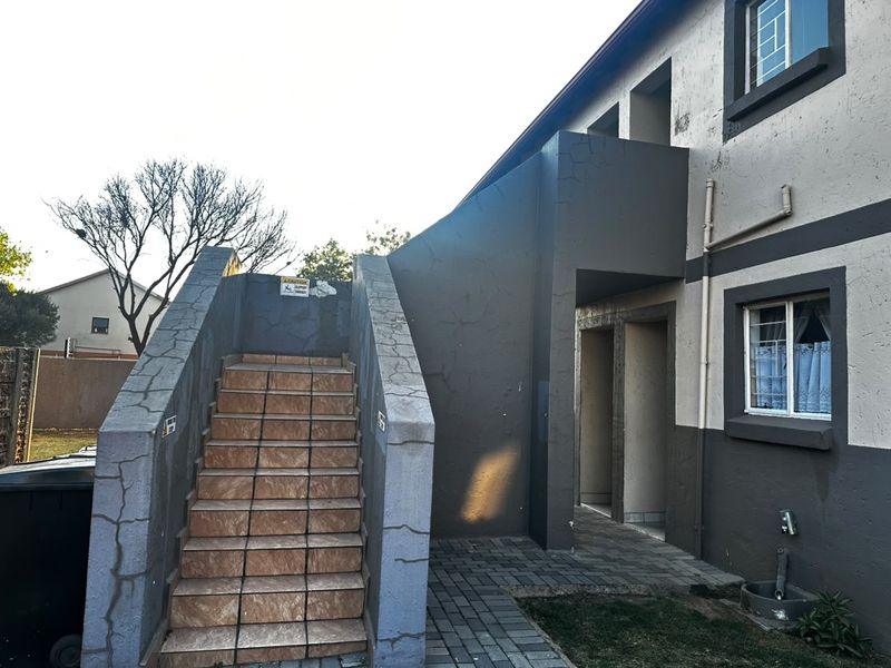 Exterior view of a townhouse rear facade featuring a tiled staircase, paved walkway, and security bars on the windows.