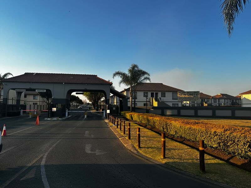 The entrance to the townhouse complex features a secure gatehouse with boom gates, paved access roads, and well-maintained perimeter landscaping.
