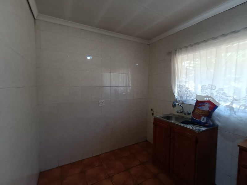A functional kitchen area featuring tiled walls, tiled flooring, and a single basin sink with wooden base cabinetry.