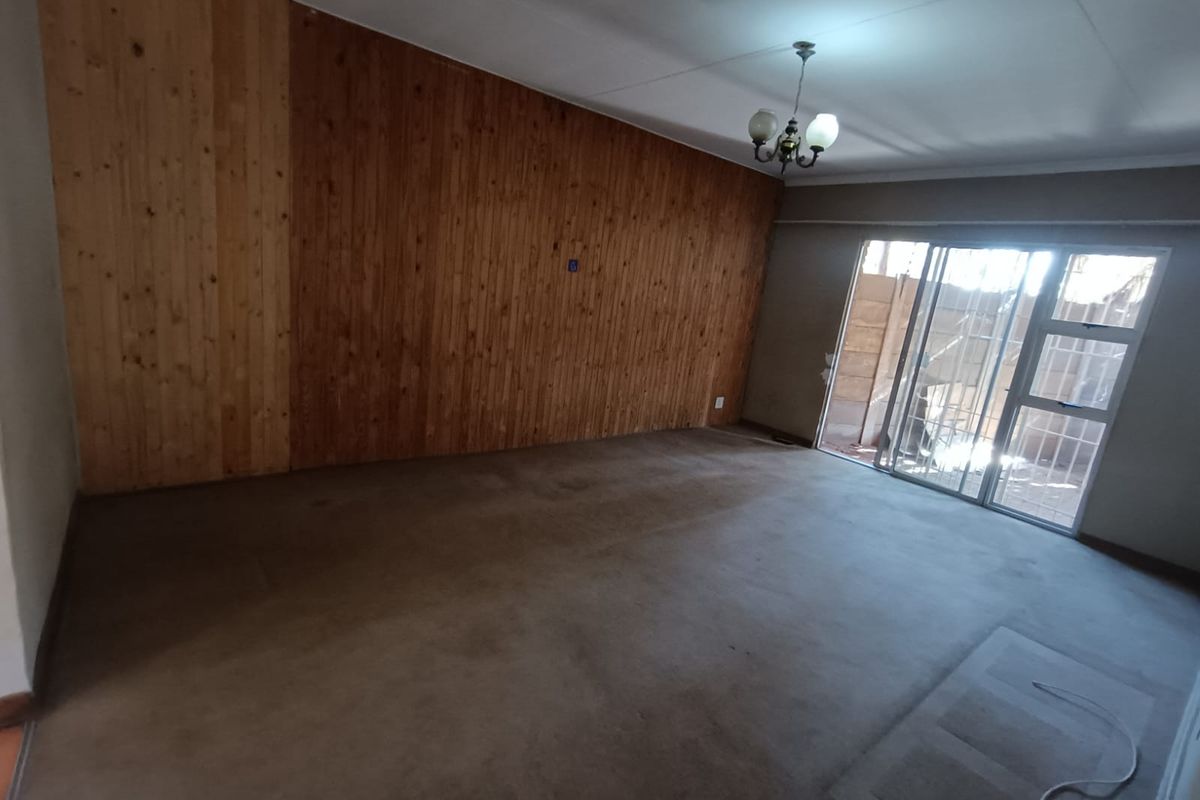 Spacious living area featuring wood paneling, carpet flooring, and a sliding glass door providing access to the exterior.