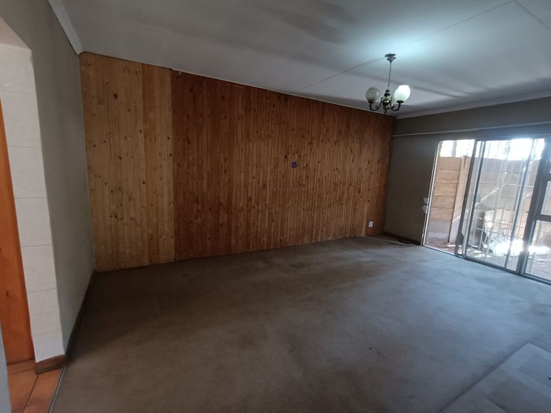 An empty living room featuring wood paneling, carpet flooring, and a sliding glass door leading to an outdoor area.