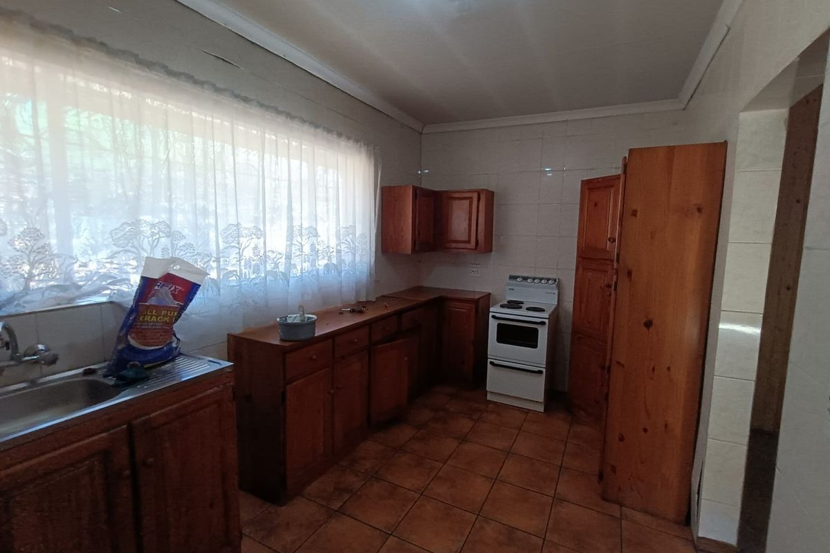 A dated kitchen featuring wooden cabinetry, tiled flooring, and a freestanding stove, offering significant potential for modernization and renovation.