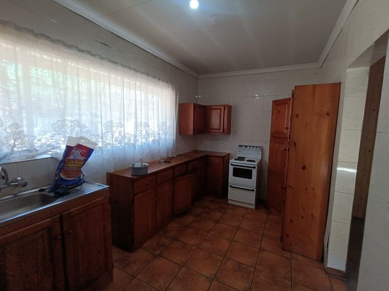 A dated kitchen featuring wooden cabinetry, tiled flooring, and a freestanding stove, offering significant potential for modernization and renovation.