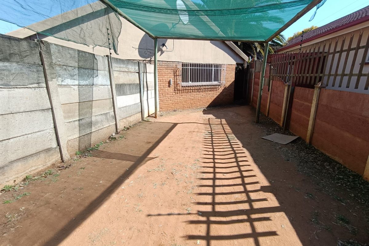 A rear outdoor area featuring a shade cloth canopy, enclosed by precast and brick boundary walls with security fencing.