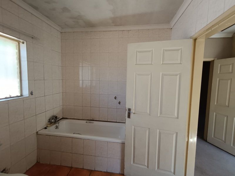A dated bathroom featuring a built-in bathtub and tiled finishes, currently empty and requiring renovation to address ceiling water damage and worn surfaces.